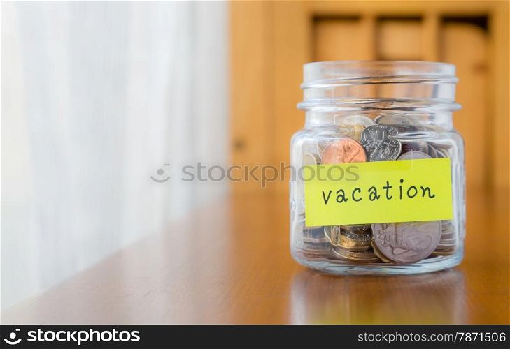 Glass bank with many world coins and vacation word or label on saving money jar