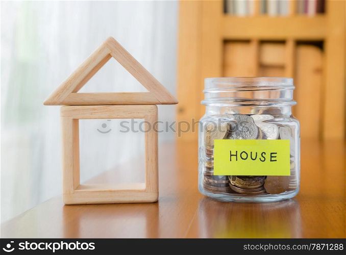 Glass bank with many world coins, house word or label on money jar and wooden home geometric blocks over table