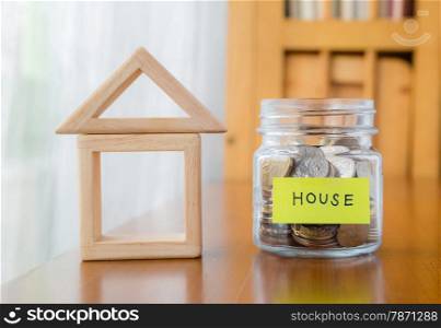 Glass bank with many world coins, house word or label on money jar and wooden home geometric blocks over table