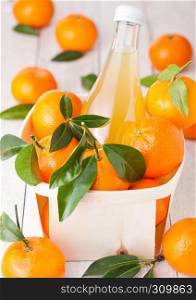 Glass bottle of fresh mandarin tangerine juice in wooden box on light wood background
