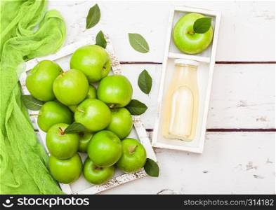 Glass bottle of fresh organic apple juice with green apples in box on wood background.