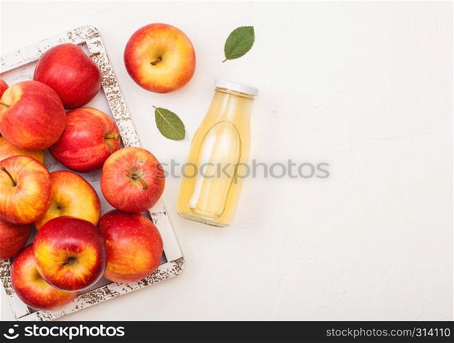 Glass bottle of fresh organic apple juice with red apples in vintage box on wood background.