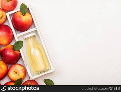 Glass bottle of fresh organic apple juice with red apples in vintage box on wood background.