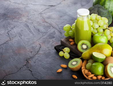 Glass bottle of fresh smoothie juice organic green toned fruit and vegetables on stone kitchen table background. With almond nuts in bowl.