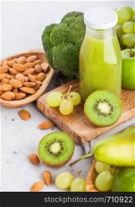 Glass bottle of fresh smoothie juice organic green toned fruit and vegetables on stone kitchen table background. With almond nuts in bowl.