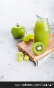 Glass bottle of fresh smoothie juice with organic green toned fruit on stone background. Apple, kiwi and grapes