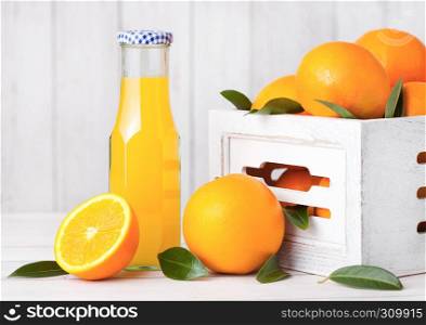 Glass bottle of organic fresh orange juice with raw oranges in white wooden box