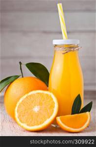 Glass bottle of organic fresh orange juice with raw oranges on light wooden background