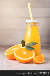 Glass bottle of organic fresh orange juice with raw oranges on light wooden background