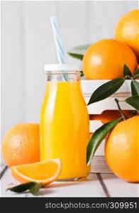Glass bottle of organic fresh orange juice with raw oranges on white wooden box