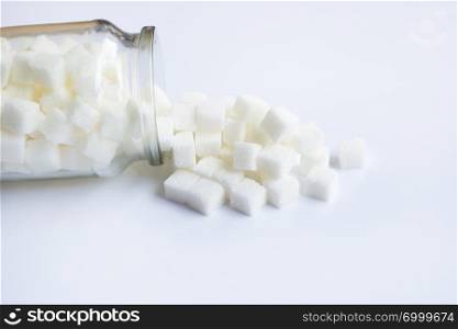 Glass bottle of sugar cubes on white background.