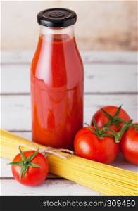 Glass bottle of tomato paste with raw spaghetti and fresh organic tomatoes on wooden background