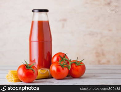 Glass bottle of tomato paste with raw spaghetti and fresh organic tomatoes on wooden background