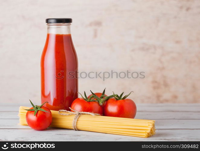 Glass bottle of tomato paste with raw spaghetti and fresh organic tomatoes on wooden background