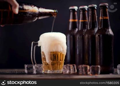 Glass bottles of beer with glass and ice on dark background