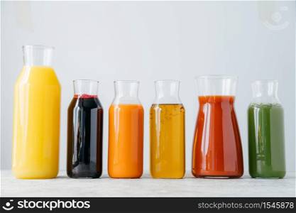 Glass bottles of fresh multicolored drinks standing in row on white background. Fruit and vegetable juice for you to drink. Healthy beverage