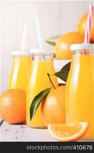 Glass bottles of organic fresh orange juice with raw oranges in white wooden box