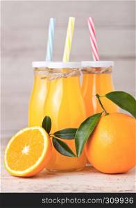Glass bottles of organic fresh orange juice with raw oranges on light wooden background
