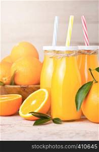 Glass bottles of organic fresh orange juice with raw oranges on light wooden background
