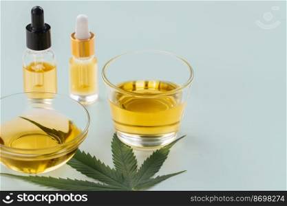 Glass bowl and bottle of CBD oil, cannabis bud, and a hemp leaf are shown of a white background. Conception of legalized oil extract from cannabis.. Glass bowl and bottle of legalized CBD oil, cannabis bud, and a hemp leaf