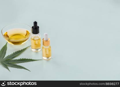 Glass bowl and bottle of CBD oil, cannabis bud, and a hemp leaf are shown of a white background. Conception of legalized oil extract from cannabis.. Glass bowl and bottle of legalized CBD oil, cannabis bud, and a hemp leaf