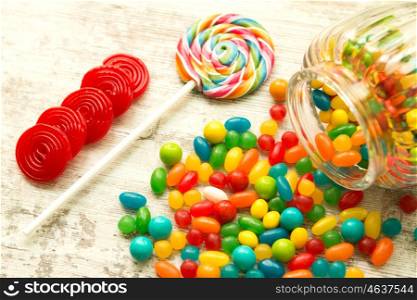 Glass bowl fallen with colorful jelly beans and a lollipop
