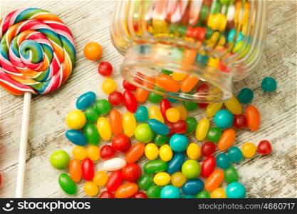 Glass bowl fallen with colorful jelly beans and a lollipop
