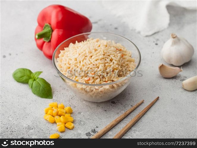 Glass bowl of boiled long grain basmati vegetable rice on light table background with sticks and red paprika with corn, garlic and basil. Macro
