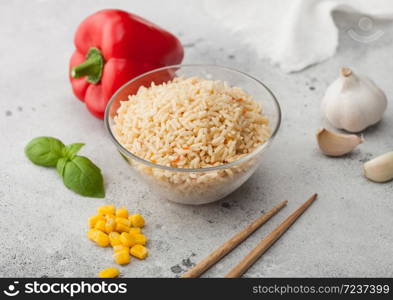 Glass bowl of boiled long grain basmati vegetable rice on light table background with sticks and red paprika with corn, garlic and basil. Macro