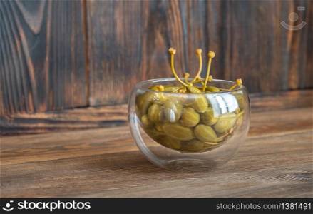 Glass bowl of capers on wooden background