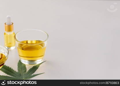 Glass bowl of CBD oil, cannabis bud, and a hemp leaf are shown of a white background. Conception of legalized oil extract from cannabis.. Glass bowl of legalized CBD oil, cannabis bud, and a hemp leaf on background.