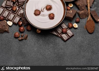 glass bowl of chocolate cream or melted chocolate, pieces of chocolate and hazelnuts on dark concrete background or table. glass bowl of chocolate cream or melted chocolate, pieces of chocolate and hazelnuts on dark concrete background