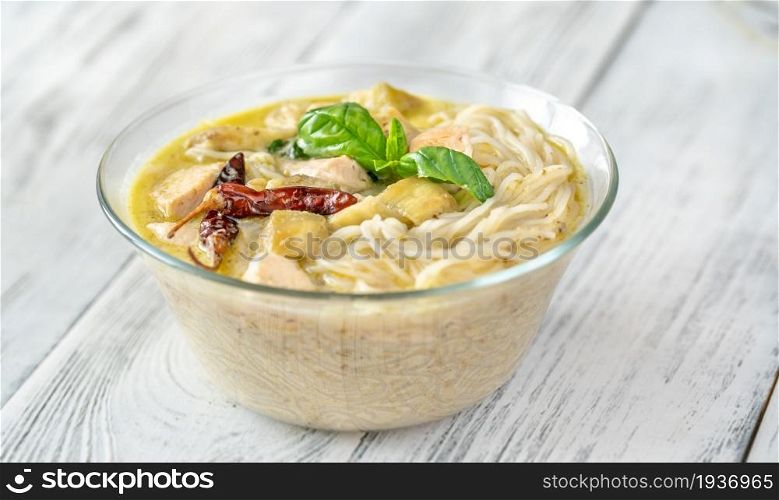 Glass bowl of green curry noodles decorated wih fresh basil