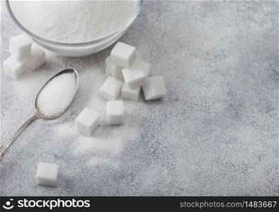 Glass bowl of natural white refined sugar with cubes and silver spoon on light background.