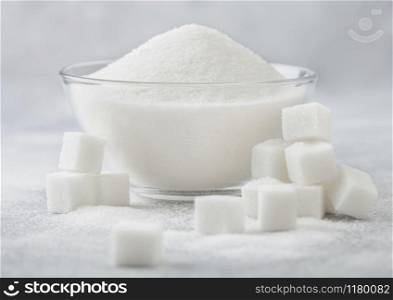 Glass bowl of natural white refined sugar with cubes on light background.