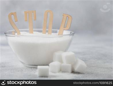 Glass bowl of natural white refined sugar with cubes on light background with STOp letters. Unhealthy food concept.