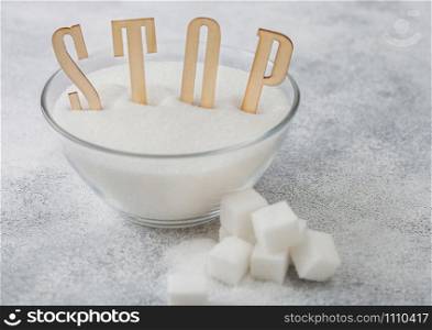 Glass bowl of natural white refined sugar with cubes on light background with STOp letters. Unhealthy food concept. Top view