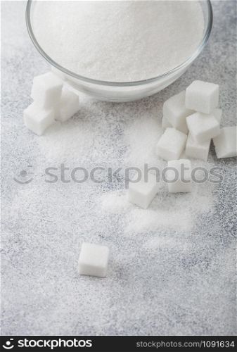 Glass bowl of natural white refined sugar with cubes on light table background. Top view