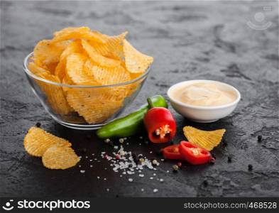 Glass bowl plate with potato crisps chips with chilli pepper on black stone background. Red and green chilli pepper with garlic and salt.
