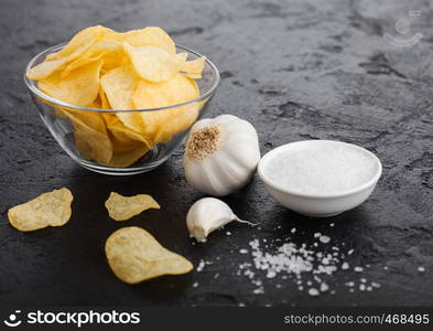 Glass bowl plate with potato crisps chips with onion flavour with garlic and salt on black stone background.