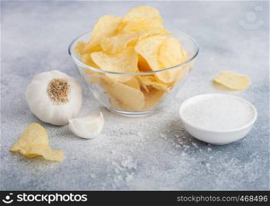 Glass bowl plate with potato crisps chips with onion flavour with garlic and salt on light background.