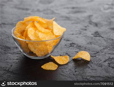 Glass bowl plate with potato crisps chips with paprika on black stone background.