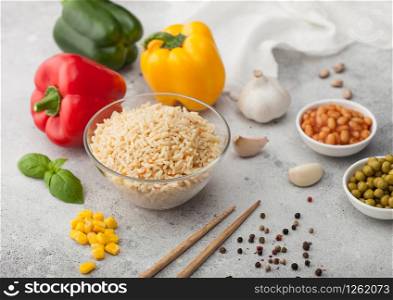 Glass bowl with boiled long grain basmati rice with vegetables on light background with sticks and paprika pepper with corn, beans and peas.