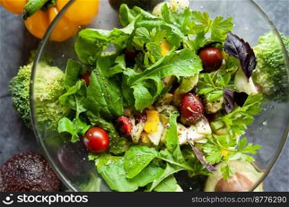 Glass bowl with fresh salad, greens, avocado and vegetables. Healthy food concept. Rustic style, top view