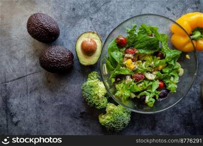 Glass bowl with fresh salad, greens, avocado and vegetables. Healthy food concept. Rustic style, top view