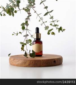 glass brown bottle with a pipette on a wooden podium and a branch of eucalyptus. Advertising and promotion of cosmetic products