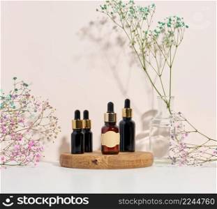 glass brown bottle with a pipette on a wooden podium and a branch of flowers. Advertising and promotion of cosmetic products