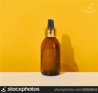 glass brown bottle with cosmetic spray on a yellow background