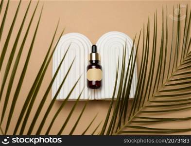 glass brown bottle with pipette and paper blank label on light brown background, near palm leaf. Mockup skincare cosmetic product