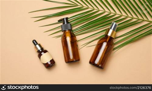 glass brown cosmetic bottles with pipette, spray and dispenser on brown background, top view. Containers for liquid products